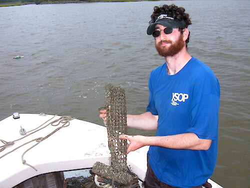 Ben Fertig poses with one of the cages he created to hold oysters for a 2 month coastal bay's nutrients exposure period.