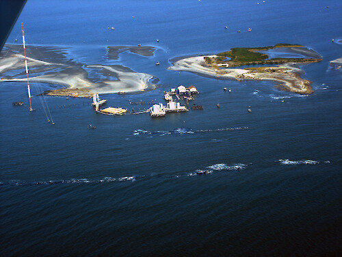 Aerial photo showing land loss inshore of protection barriers and subsequent flooding of facilities
