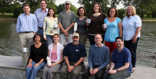 Jane Hawkey poses for a group photo with her colleagues in front of a river. Photo credit Simon Costanzo