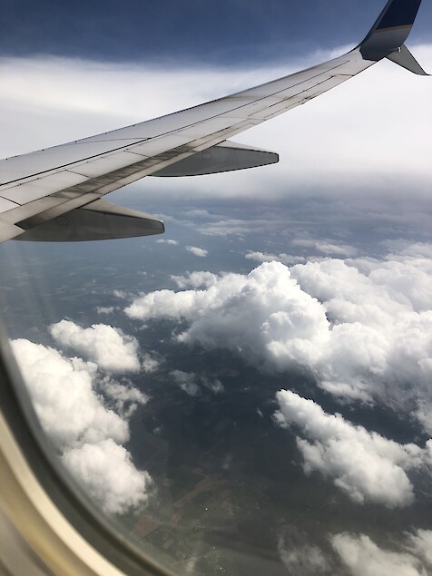 The right-hand wing of an airplane and beyond to a cloudy, green Maryland landscape as viewed through the airplane window.