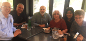 Six people sit around a restaurant table smiling at the camera. 