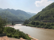 View of the Chishui River flowing at the base of two hills around a bend and under a bridge.