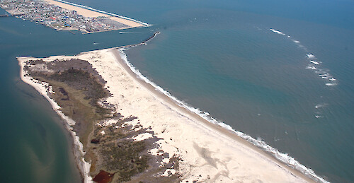 Looking north, showing the northern end of Assateague Island, the Ocean City Inlet, and the southern end of Fenwick Island and Ocean City. Also visible is the ebb tidal shoal, indicated by the waves breaking offshore.
