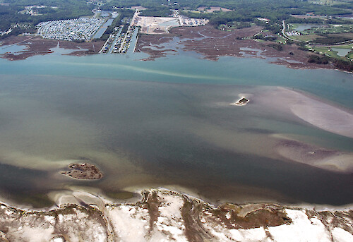 Looking west across Sinepuxent Bay. The inland edge of Assateague Island is visible in the foreground. Also visible are seagrasses and shoals in the bay, and canal developments, ditches, and golf courses in the background.