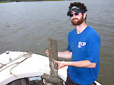 Ben Fertig poses with one of the cages he created to hold oysters for a 2 month coastal bay's nutrients exposure period.