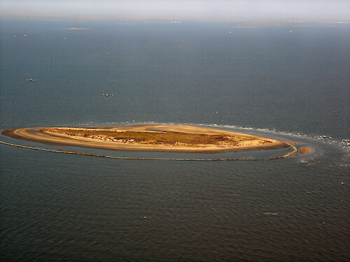 Aerial photo of small island with extensive protection barrier, showing continued erosion and movement of sand 