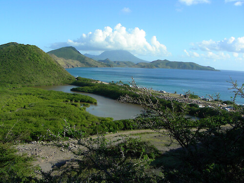 Southeast of Basseterre is a salt pond with a barrier strip of sand, popular with tourists, along Frigate Bay. Beyond the curve of the bay is a distant view of the island of Nevis with its volcanic mountain top in cloud.