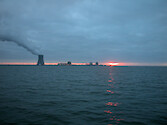 Nuclear power plant chimney spews smoke or steam on a cloudy evening.