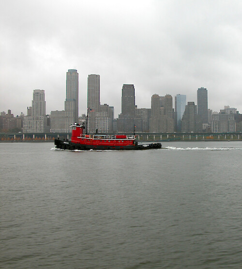 The grey sky, grey skyline, and grey water did not wash out the bright color of this red tugboat.