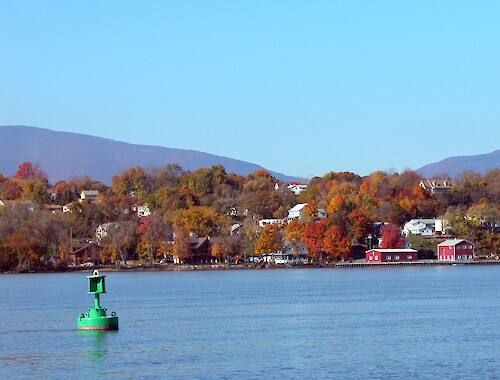 Green navigational buoy floats in tidal current in front of rural Catskill town.