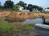 On a property that was grandfathered to build on a tiny waterfront lot, the owner was allowed by the local zoning department to fill in a low wetland where his well (white pipe) and dock electric service (right center of photo) were located. As this photo documents, this low area was frequently flooded.