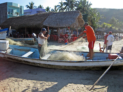 Local fishermen preparing their nets. This style of open boat with an outboard motor is called a panga, and is hauled up on to the beach when not in use.