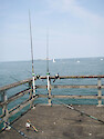 Fishing rods line the fishing pier at the Chesapeake Bay Bridge Tunnel in Virginia. The tunnel lies in front of the pier and emerges from the rock island beyond the sailboats in the background.