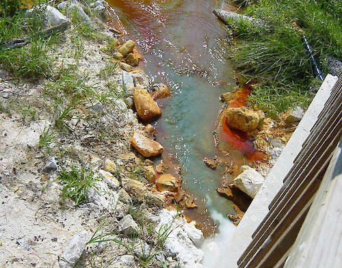 Acidic mine tailings are being mitigated by the addition of alkaline chemicals (white), entering the stream below the wooden structure. 