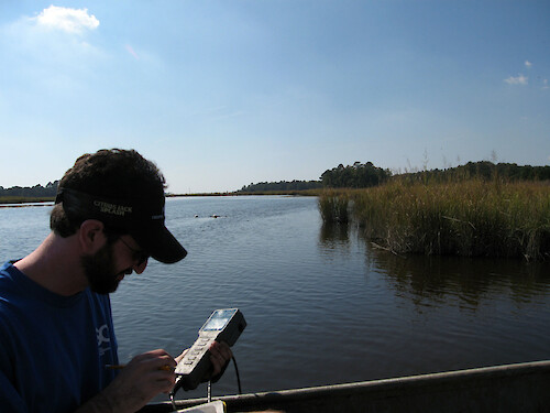 Monitoring water quality with a YSI 85 instrument in Monie Creek, part of the Chesapeake Bay National Estuarine Research Reserve. Buoys marking oyster biological indicators can be seen in the background.