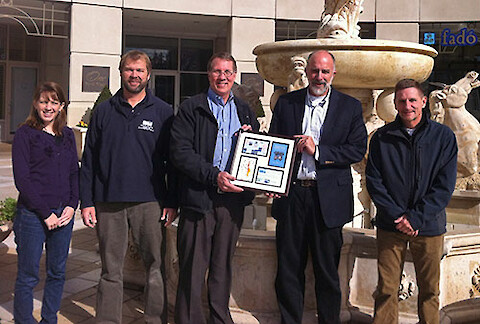 Caroline Wicks, Heath Kelsey, Russell Callender, Bill Dennison, and Ken Barton with a framed history of EcoCheck's first phase.
