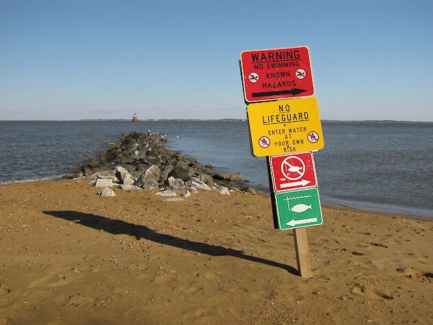 A sign posted next to the Chesapeake Bay reads “Warning No Swimming Known Hazards.”