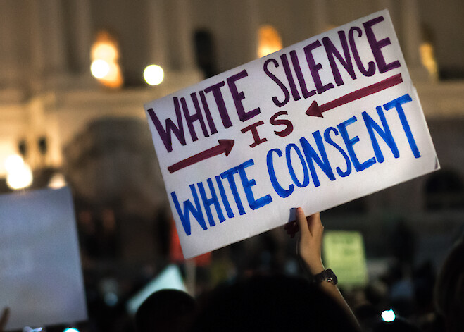 A Black Lives Matter protest sign is held by a person in the crowd at a rally in front of the White House.