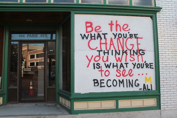 Social justice graffiti message that quotes Muhammad Ali is on a boarded-up window of a building.