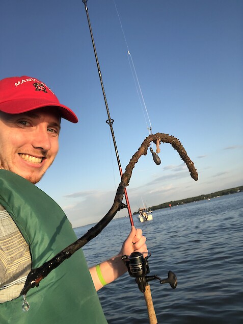 Joe Edgerton is smiling as he holds up his fishing pole to showcase a muddy twig that was caught at the end of the hook.