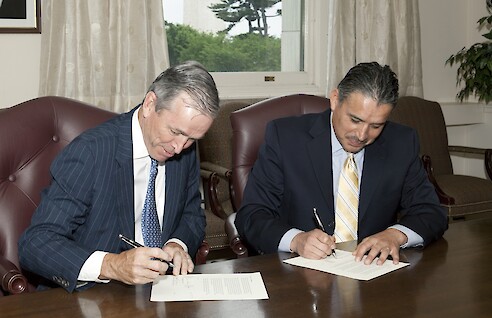A photograph of two men signing paperwork.