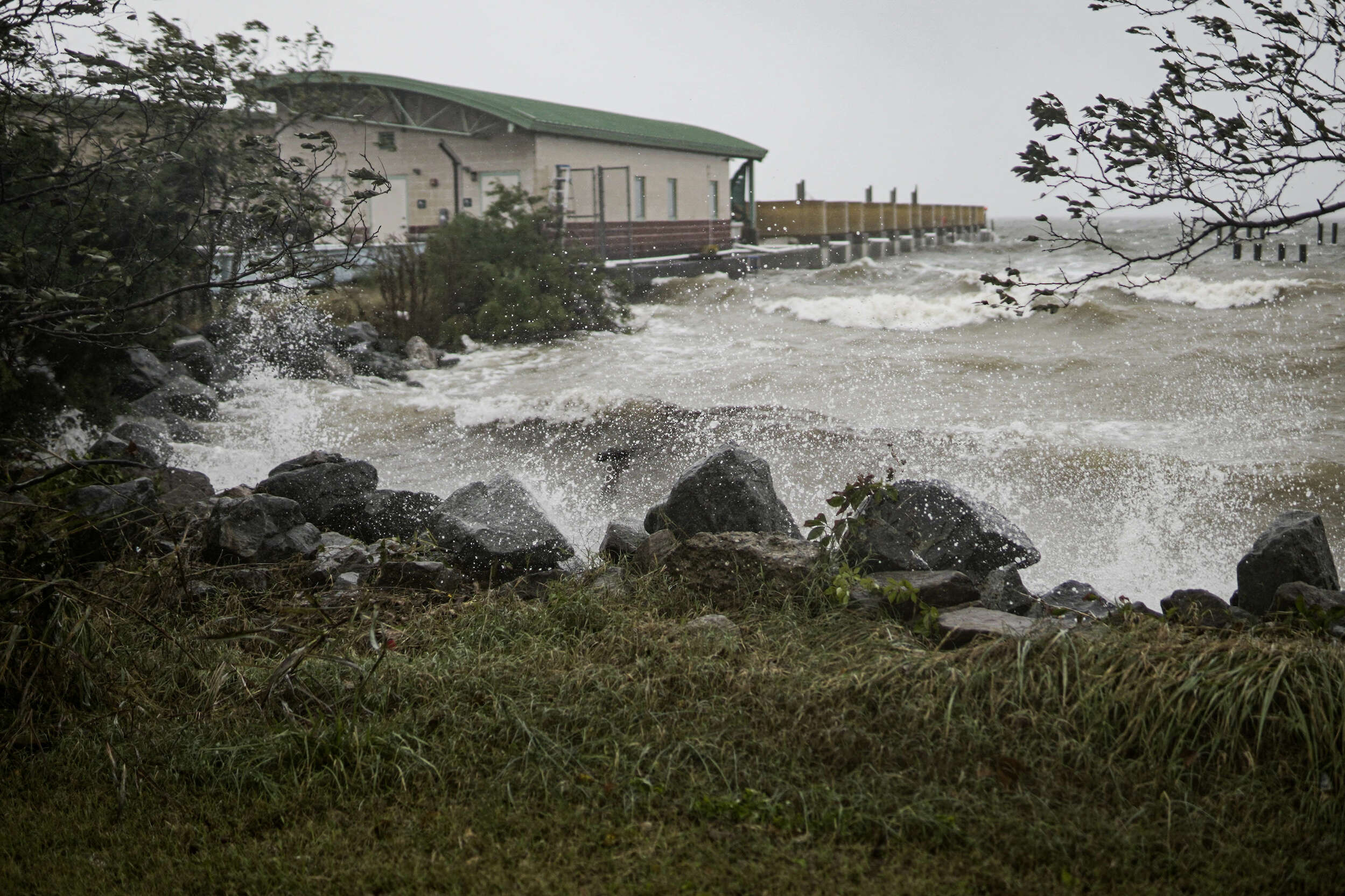 Murky Choptank River waves crash against a rocky shoreline with part of the oyster hatchery building to the side.