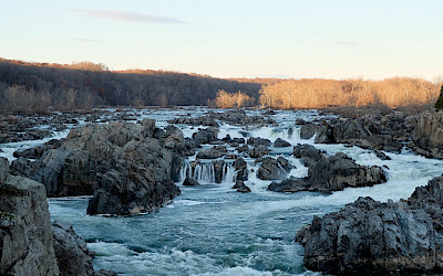 An image of a wide and rocky white-water section of the Potomac, with the water rushing over and between jagged boulders.