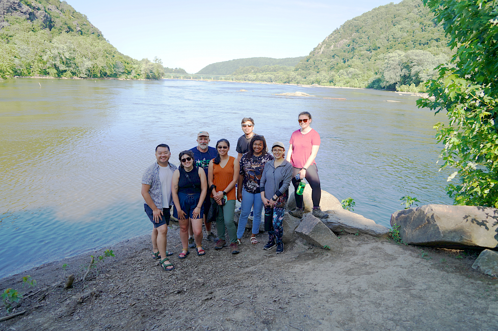 A group of 8 people from the COAST Card team stand on the river bank with the view of the two rivers behind them.