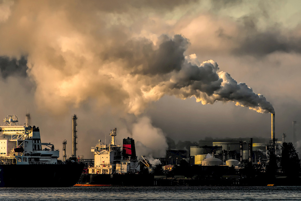 A smokestack at an industrial port pours smoke into the air.