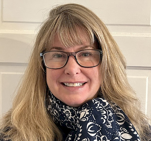 Headshot of Stacy wearing glasses and a blue, floral patterned scarf.