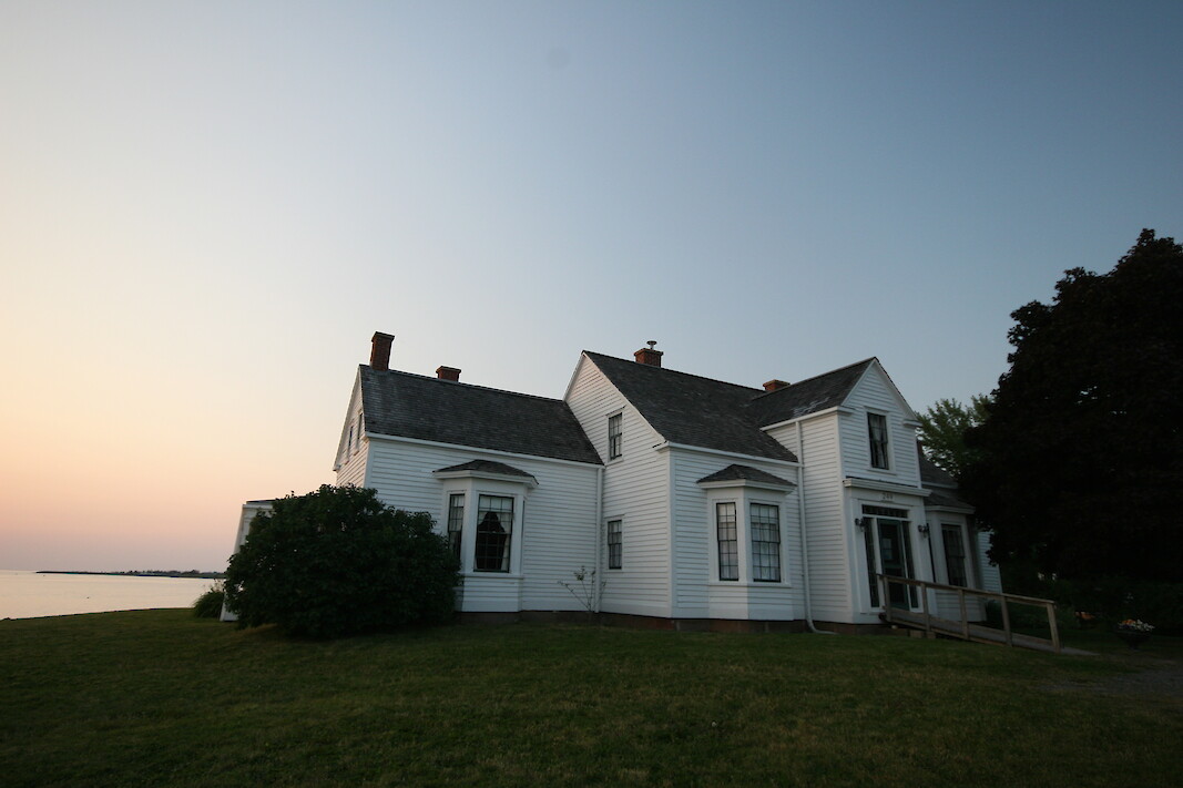 The white Thinkers Lodge building sits by the coast of Northumberland Strait partially illuminated by the sunset.